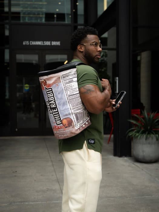 An athlete outside an office building with a large White Rabbit Energy bag over one shoulder